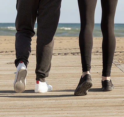 Dos personas caminando juntas por una pasarela de madera hacia la playa, simbolizando el camino y la historia compartida de dos nietos de españoles retornados.