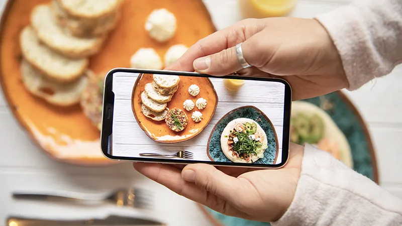 Manos sosteniendo smartphone fotografiando platos de comida para Instagram restaurantes