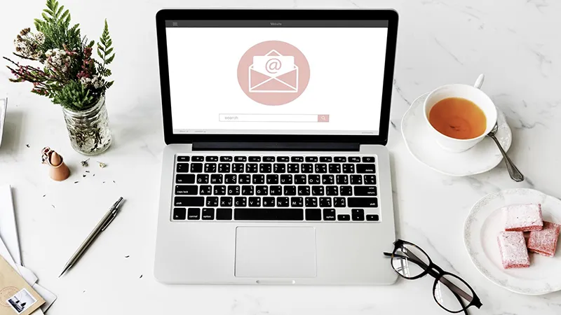 Ordenador portátil mostrando un icono de correo electrónico en una mesa, ilustrando una estrategia de email marketing para restaurantes.