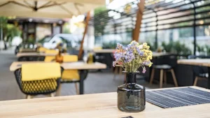 Mesa de madera con un jarrón de flores en la terraza de un restaurante, preparada para recibir clientes en la temporada alta.
