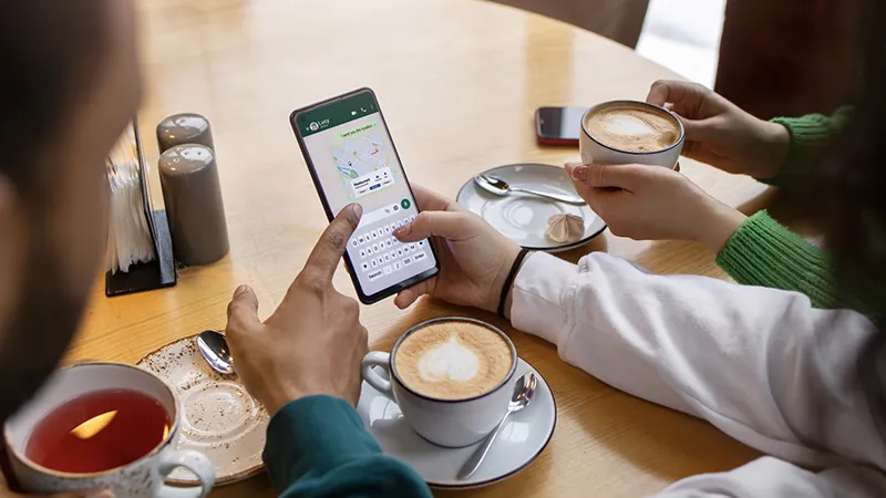 Cliente usando la aplicación de mensajería en su móvil mientras toma un café, un ejemplo visual del uso de WhatsApp Business para hostelería.