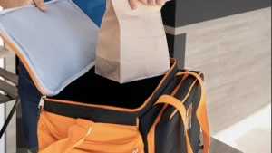 Empleado guardando un pedido en una mochila térmica de reparto, un paso clave para el éxito de un restaurante en apps de delivery.