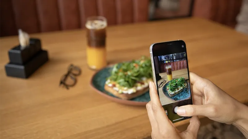 Persona haciendo una foto con su smartphone a una tostada de aguacate y rúcula con un café en la mesa de un restaurante.