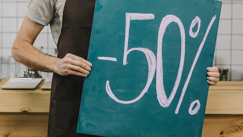 Camarero con delantal sosteniendo un cartel de pizarra con un descuento del 50% escrito a tiza